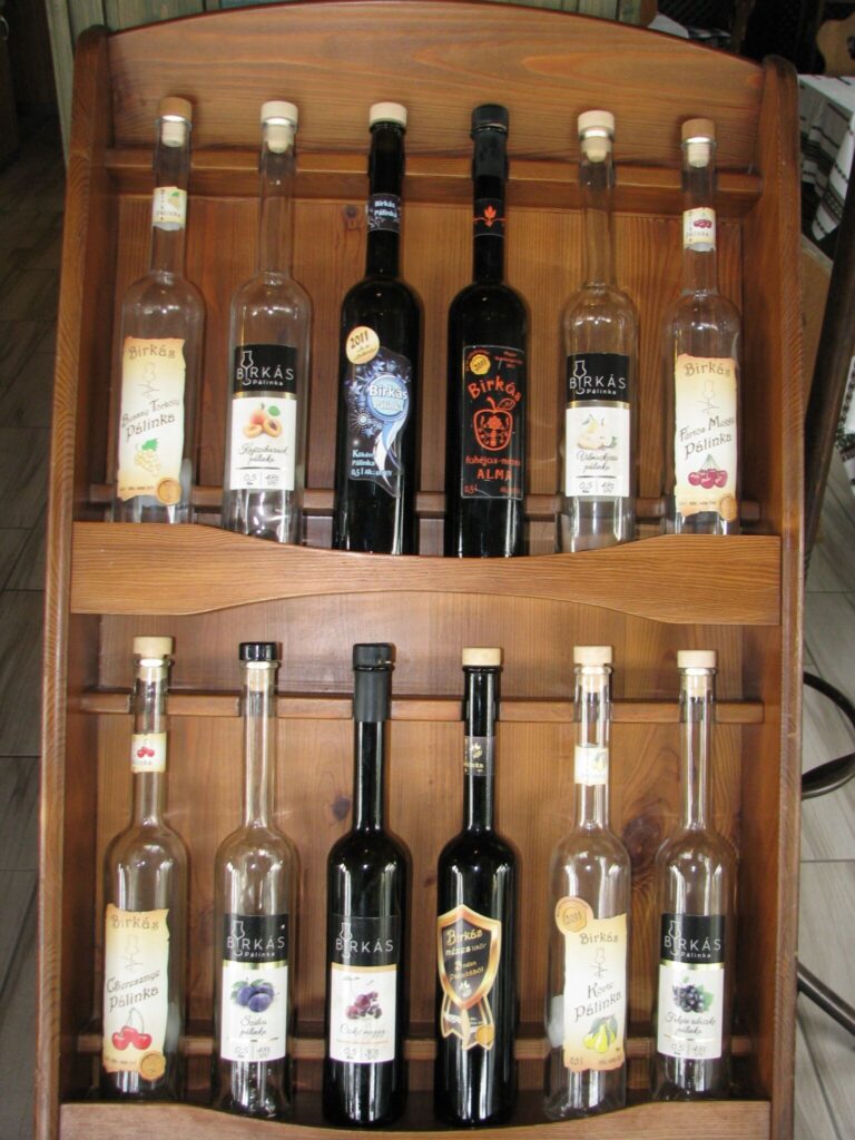 Különböző ízesítésű pálinkás üvegek egy fából készült polcon.